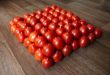 A neatly arranged pyramid of fresh red tomatoes on a wooden floor, showcasing vibrant natural colors.