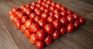 A neatly arranged pyramid of fresh red tomatoes on a wooden floor, showcasing vibrant natural colors.